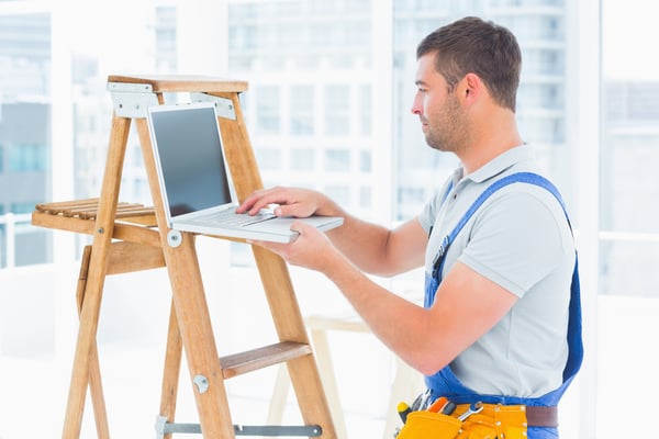 Side view of handyman using laptop by step ladder in bright office